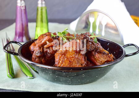 Pollo con prugne cotte al forno in un recipiente di colore nero su uno sfondo di materie tessili. Foto Stock