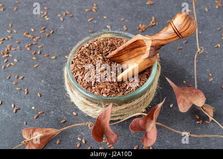 Una ciotola di vetro di semi di lino con scoop di oliva circondato da fiori artificiali su un grigio Sfondo astratto. Mangiare sano concetto. Foto Stock