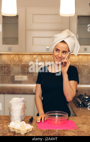 Piacevole donna allegra parlando al cellulare e per la cottura Foto Stock