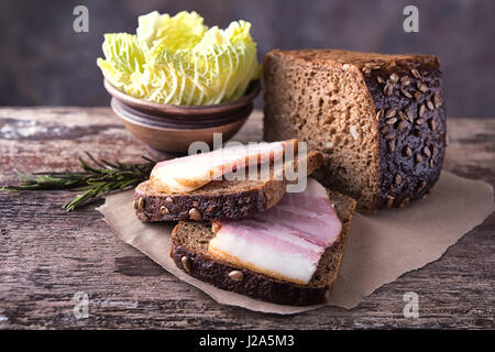 Tradizionali ucraine sandwich fatti di marrone pane di segale e lardo affumicato su un pezzo di carta marrone e legno naturale superficie testurizzata con unfocused Foto Stock