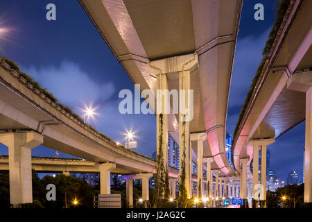 Cina, Shanghai, torreggianti cavalcavia di Yan'an Expressway con lo skyline della città di distanza sulla serata di autunno Foto Stock