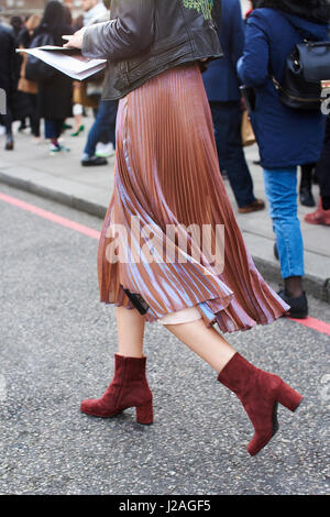Londra - febbraio, 2017: sezione bassa della donna a piedi indossando chiffon gonna plissettata con pelle scamosciata marrone stivaletti in strada durante la London Fashion Week, verticale, vista laterale Foto Stock