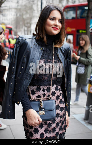 Londra - febbraio, 2017: tre quarti di lunghezza vista di moda donna che indossa un nero Abito in pizzo con la giacca di pelle sulle spalle e un Valentino corpo a croce borsetta in piedi la Street, London Fashion Week, giorno 5. Foto Stock