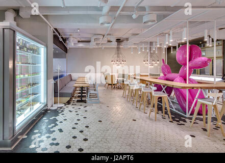 Pasticceria in stile loft con luce interiore. Ci sono scaffalature in legno con sedie attorno a big pink cane gonfiabile, poltrone, tavoli, divani, lumino Foto Stock