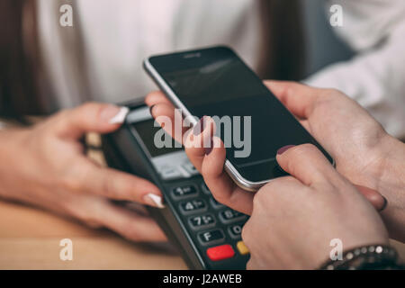 Dettaglio immagine di donna con smart phone a pagare al bancone Foto Stock