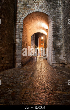 Strada di ciottoli e illuminata gate nella città vecchia di Girona a notte, Catalogna, Spagna Foto Stock