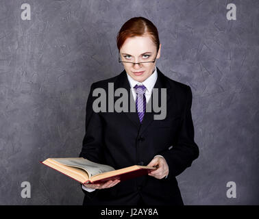 Avvocato femmina legge un grande libro con espressione seria, donna in un uomo la tuta, cravatta e occhiali di protezione Foto Stock