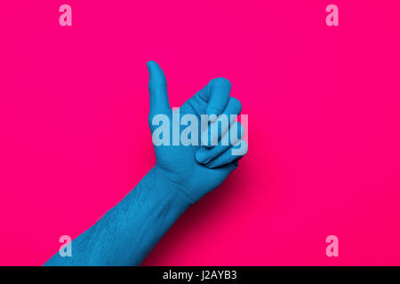 Close-up di blu dipinto a mano pollice gesti fino contro sfondo rosa Foto Stock