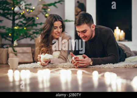 Coppia sorridente un caffè mentre giaceva sul tappeto a casa durante il periodo di Natale Foto Stock