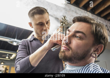 Basso angolo vista del parrucchiere maschio giovane di taglio del cliente a capelli barbiere Foto Stock