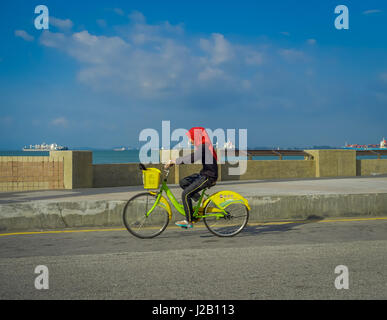 George Town, Malesia - 10 Marzo 2017: bella vista panoramica di sconosciuti donne musulmane in bicicletta lungo l'Esplanade, una posizione di fronte al mare nel cuore della citta'. Foto Stock