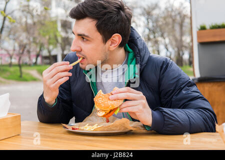 L'uomo mangiare patate fritte con un hamburger in street food cafe Foto Stock