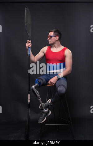 Un giovane uomo adulto solo, in seduta sgabello da bar, atleta sporstman canoe kayak paddle, gamba protesico, disattivato Foto Stock