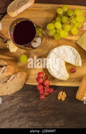 Un overhead foto di un bicchiere di vino rosso con una selezione di formaggi, pane, uva e un posto per il testo Foto Stock