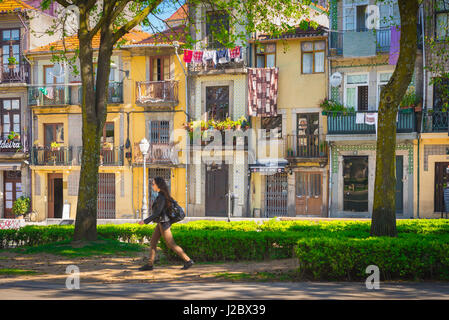 Porto Portogallo parco, vista di una donna che cammina attraverso i giardini Cordoaria, passato una strada che contiene una fila di colorate case a schiera, Porto Europe. Foto Stock