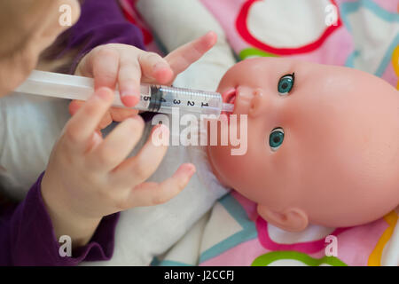 Bambina riproduzione medico con una bambola e l'applicazione di farmaci con la siringa e la cura di una bambola, concetto di maternità, stile di vita e dell'infanzia Foto Stock