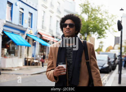 Elegante giovane uomo a camminare lungo la strada trafficata Foto Stock