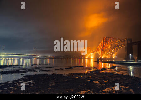 Il Ponte di Forth Rail illuminata di notte. Luce dorata colpisce le nuvole sopra. South Queensferry, Edimburgo, Scozia Foto Stock