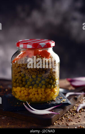 Una insalata fatta con il mais dolce, i piselli, la quinoa e carota servita in un barattolo di mason, in differenti stabilisce, posto su una tavola in legno rustico Foto Stock