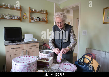 Signora anziana preparare un tè inglese con vari tipi di torte sul suo tavolo da cucina, England, Regno Unito Foto Stock