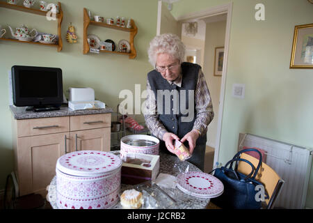 Signora anziana preparare un tè inglese con vari tipi di torte sul suo tavolo da cucina, England, Regno Unito Foto Stock