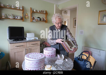 Signora anziana preparare un tè inglese con vari tipi di torte sul suo tavolo da cucina, England, Regno Unito Foto Stock