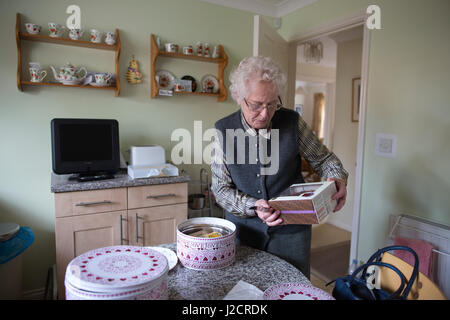 Signora anziana preparare un tè inglese con vari tipi di torte sul suo tavolo da cucina, England, Regno Unito Foto Stock