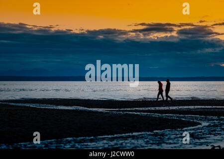 Paio di passeggiare lungo la spiaggia in un cupo, NUVOLOSO TRAMONTO cielo in Puget Sound di Seattle. In pochi, troviamo la pace dalla turmoils siamo in vita. Foto Stock