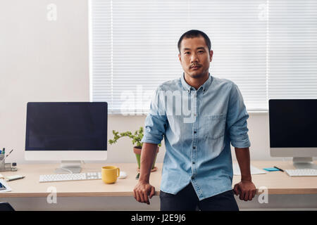 Focalizzato designer asiatici appoggiato su una scrivania in un ufficio Foto Stock