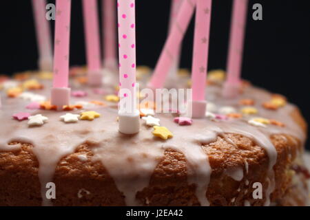 Vista ravvicinata di una celebrazione torta, con glassa, centinaia e migliaia di decorazione, e candele rosa su sfondo nero Foto Stock