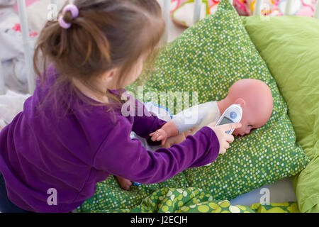 Bambina riproduzione medico con una bambola, la misurazione della temperatura con termometro elettronico e di prendersi cura di una bambola, concetto di maternità, lifestyle e c Foto Stock