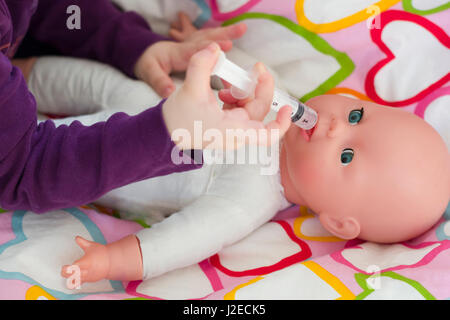 Bambina riproduzione medico con una bambola e l'applicazione di farmaci con la siringa e la cura di una bambola, concetto di maternità, stile di vita e dell'infanzia Foto Stock