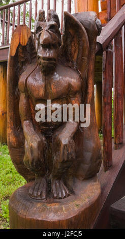 Legno gargoyle alato scultura su per le scale che portano all'entrata principale su un cottage in stile Home log in estate. Foto Stock