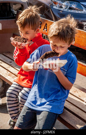 Due fratelli affamati mangiare ricoperta di cioccolato banane congelate su un marciapiede banco in Newport Beach, CA. Foto Stock