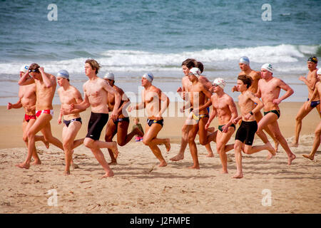 Multirazziale giovane adulto concorrenti per l'estate bagnino lavori in Newport Beach, CA, dare loro tutti come la loro esecuzione/nuoto qualifica evento inizia sulla spiaggia. Foto Stock