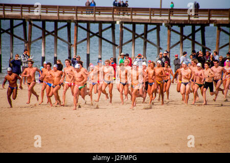 Multirazziale giovane adulto concorrenti per l'estate bagnino lavori in Newport Beach, CA, dare loro tutti come la loro esecuzione/nuoto qualificazioni inizia sulla spiaggia. Nota pier in background. Foto Stock