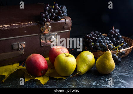 Frutte mature mele, pere e diversi giallo Foglie di autunno sul marmo scuro dello sfondo. L'uva matura nel cestello giallo e il vecchio caso sul retro dello sfondo. Foto Stock