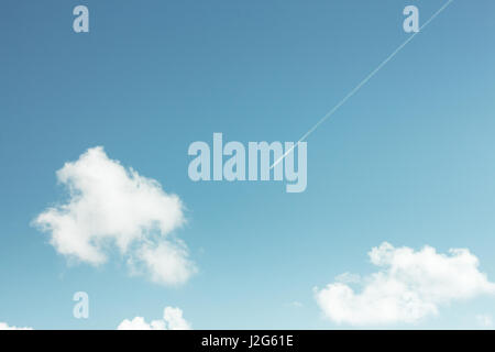 La contrail di un aereo commerciale strisce su un teal blu cielo con pochi puffy tempo equo cumulus nubi. Preso dal livello del suolo. Foto Stock