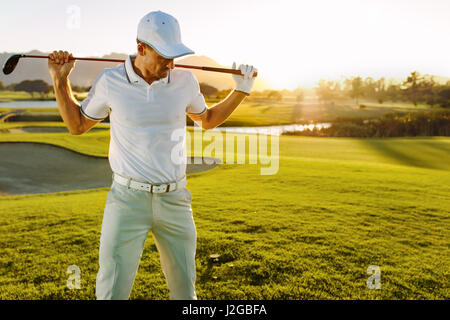 Colpo di golfista maschio con golf club in corso su un giorno d'estate. Giovane uomo tenendo un golf club e guardando verso il basso. Foto Stock