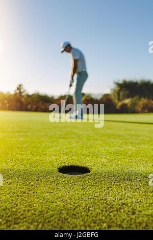 Colpo verticale del foro di golf nel campo verde con il golfer in background. Giocatore di Golf mettendo la sfera nel foro. Foto Stock