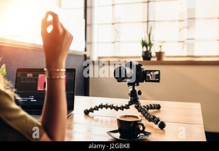 Vlogger femmina guardando la fotocamera mentre per editing video sul suo computer portatile. Giovane donna che lavorano su computer con caffè e la fotocamera sulla sua scrivania. Foto Stock