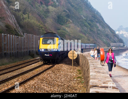 Un treno passa walkers sul Teignmouth fronte mare. Foto Stock