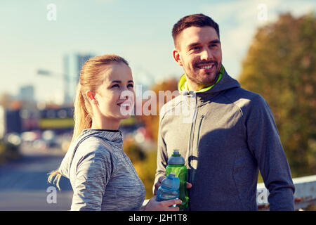 Coppia sorridente con bottiglie di acqua all'aperto Foto Stock