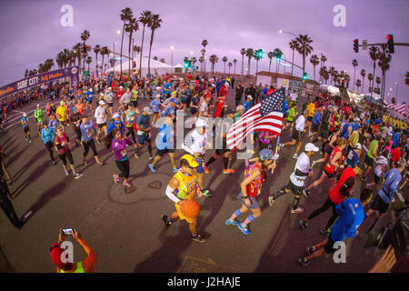 Multirazziale prima maratona-calore concorrenti di lasciare la linea di partenza di prima mattina in Huntington Beach, CA, colloquialmente noto come 'Surf città." Nota bandiera americana portato da runner. Foto Stock