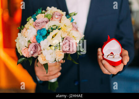 Proposta di matrimonio - confezione regalo rossa con anello di nozze e bouquet nelle mani dell'uomo. Foto Stock