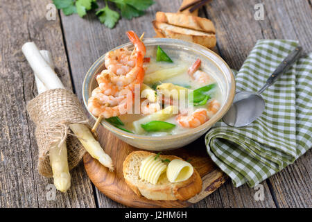 La Crema di zuppa di asparagi con i gamberi fritti e neve piselli, servita con crostini di baguette con burro rotoli Foto Stock