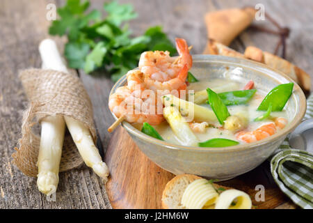 La Crema di zuppa di asparagi con i gamberi fritti e neve piselli, servita con crostini di baguette con burro rotoli Foto Stock