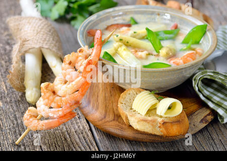 La Crema di zuppa di asparagi con i gamberi fritti e neve piselli, servita con crostini di baguette con burro rotoli Foto Stock