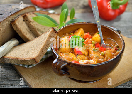 Hot vegetariano gulasch di patate servita in una ciotola di ceramica con deliziosi scuro agriturismo cotto il pane su un vecchio tavolo di legno, una tirolese specialità di montagna Foto Stock