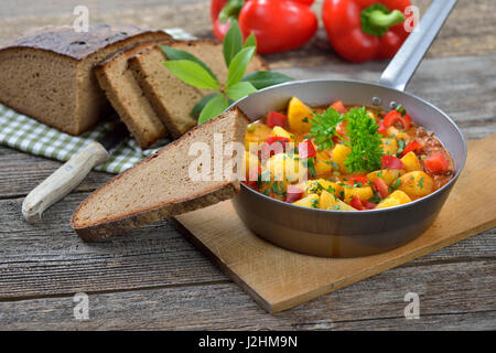 Hot vegetariano gulasch di patate servita in una padella di ferro con deliziosi scuro agriturismo cotto il pane su un vecchio tavolo di legno, una tirolese specialità di montagna Foto Stock